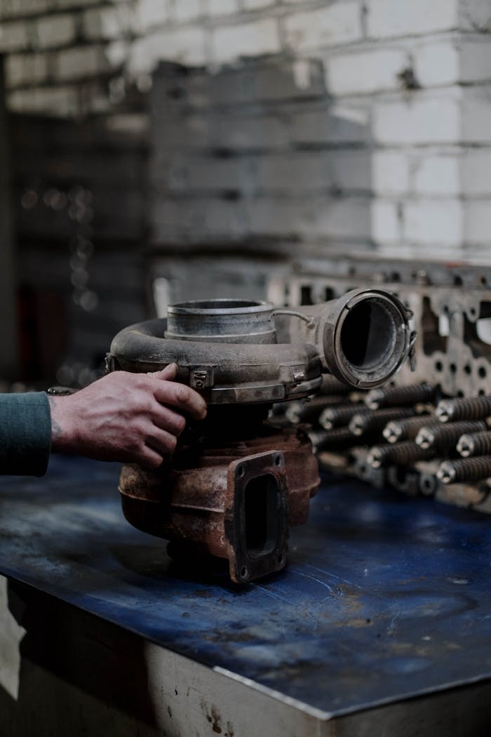 A close-up of a mechanic's hand holding a turbocharger on a workbench in a workshop.