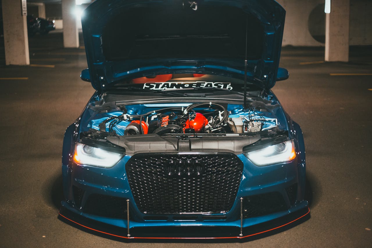 Blue sports car with open hood displaying engine in dimly lit urban setting.